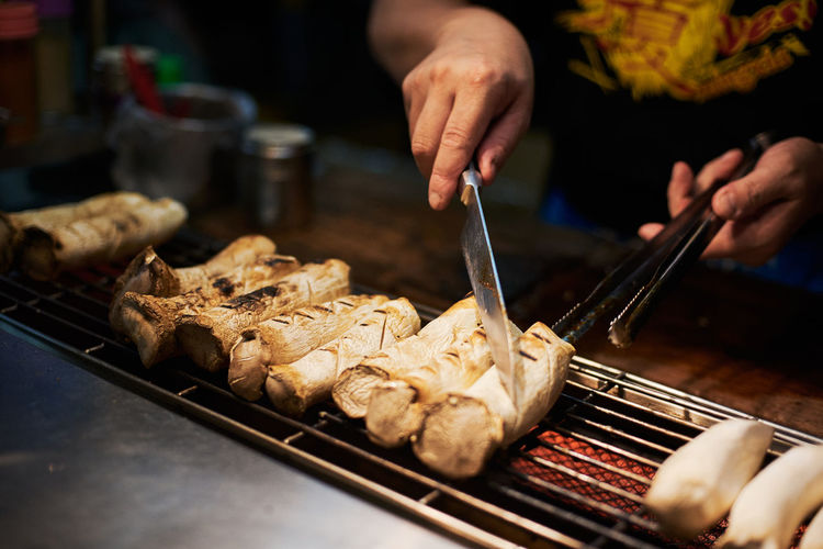 Close-up of man preparing food - baked mushrooms in night market in asia