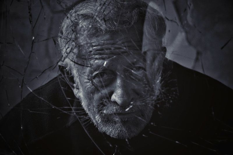 Close-up portrait of mature man seen through cracked window