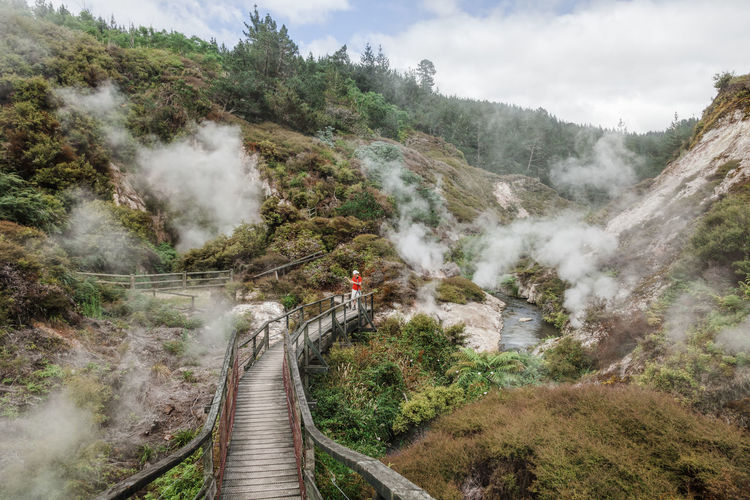 Man photographing hot spring while standing on footbridge on mountains