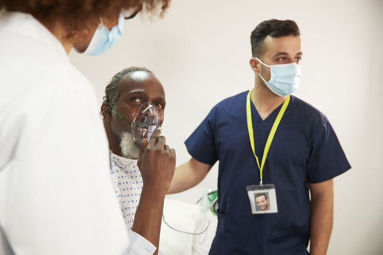 Patient adjusting oxygen mask looking at doctor in medical room