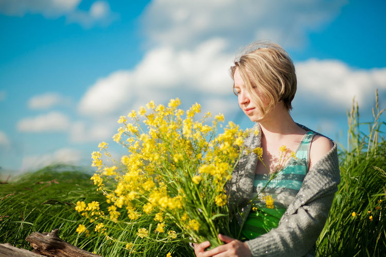 Young woman looking at camera while standing by plants against sky