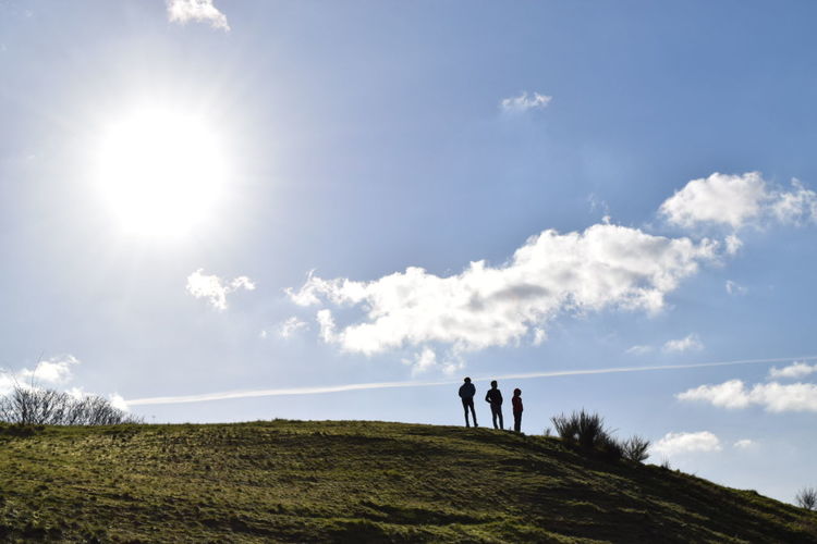 Low angle view of silhouette friends standing on grassy hill