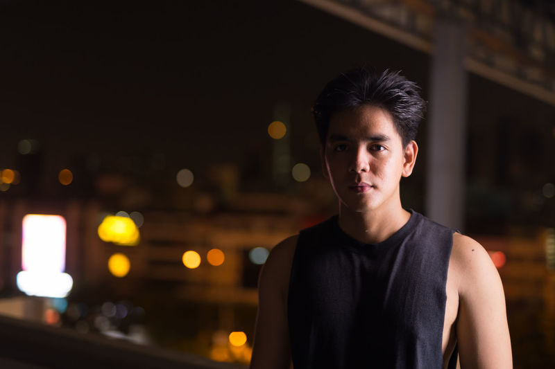 Portrait of young man standing in city at night