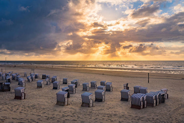 Hooded chairs on beach against sky during sunset, at the island norderney 