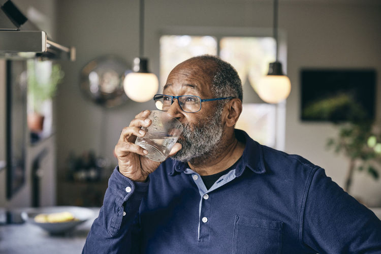 Contemplative senior man drinking water at home