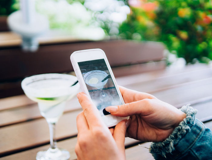 Close-up of woman photographing drink and table through mobile phone