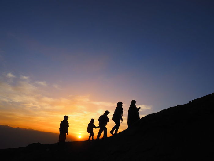 Silhouette people on mountain against sky during sunset