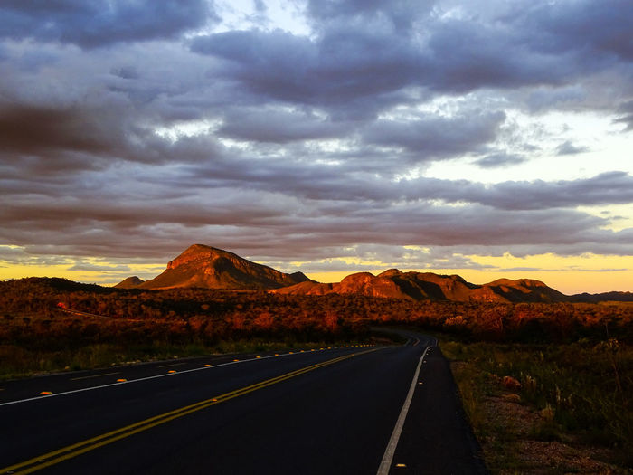 Empty road by mountains against sky during sunset