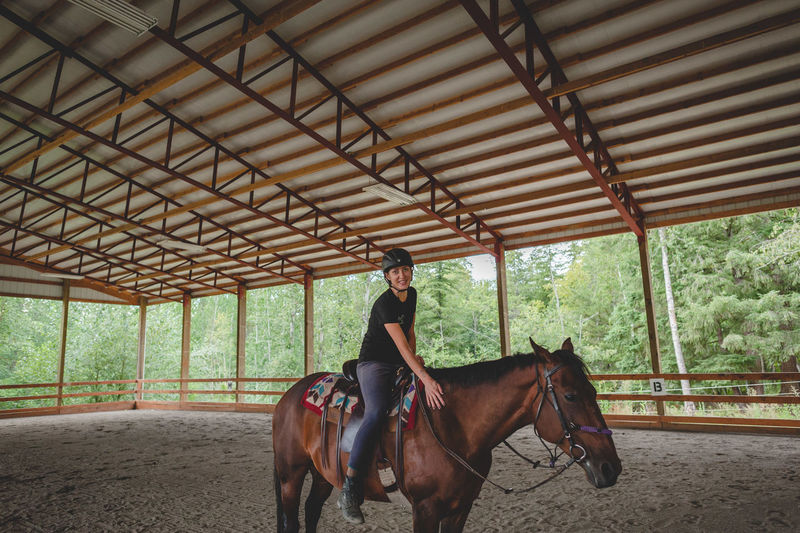 Portrait of young woman riding horse at barn