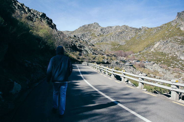 Rear view of man walking on road against mountain