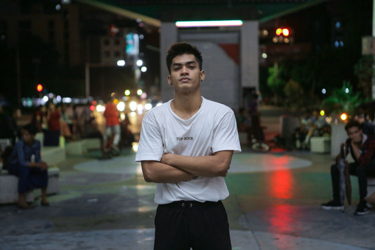 Young man with arms crossed while standing in city at night