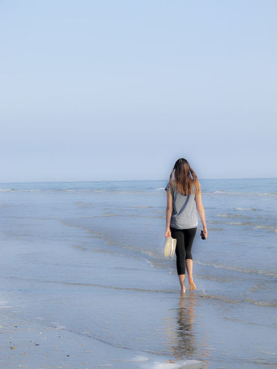 Rear view of woman walking on shore at beach against clear sky