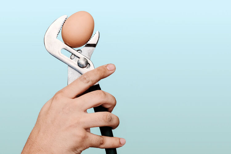 Close-up of person hand holding a spanner against white background