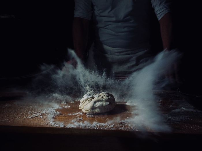 Midsection of mid adult man kneading dough on table in darkroom