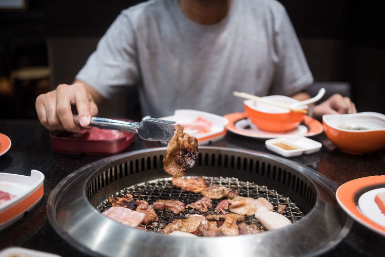Midsection of man cooking meat on barbecue grill in restaurant