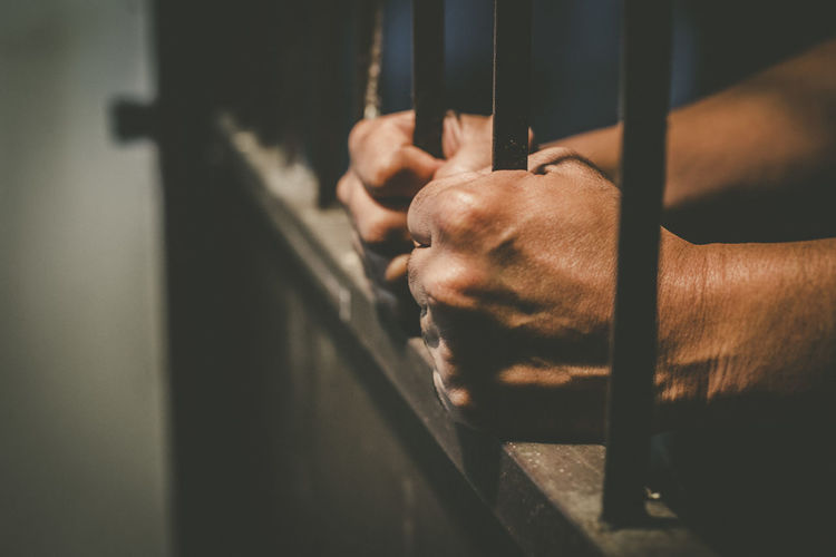 Cropped hands of male prisoner holding prison bars