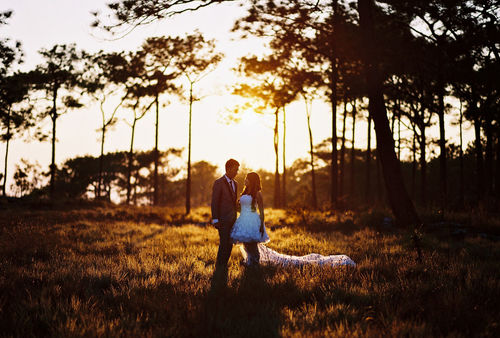 Couple standing on field against sky during sunset