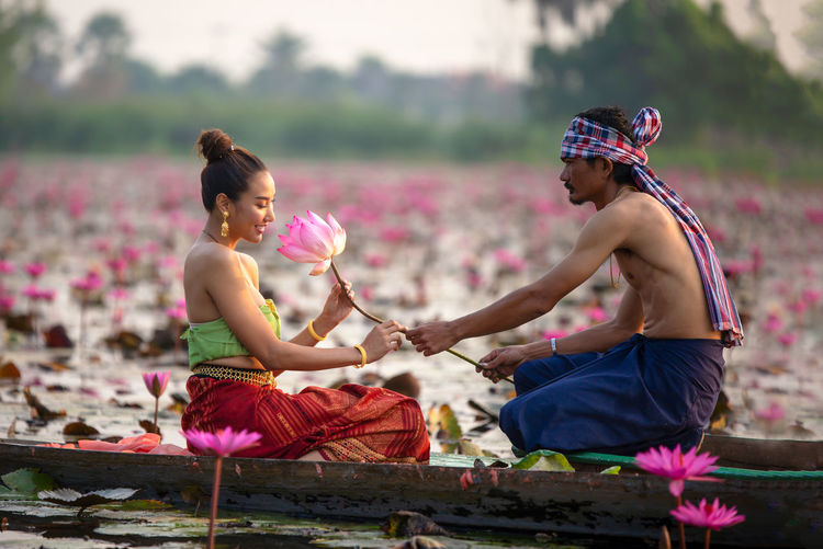 Side view of man giving lotus to woman on boat in lake