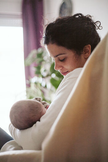 Close-up of smiling mid adult woman breastfeeding newborn girl at home