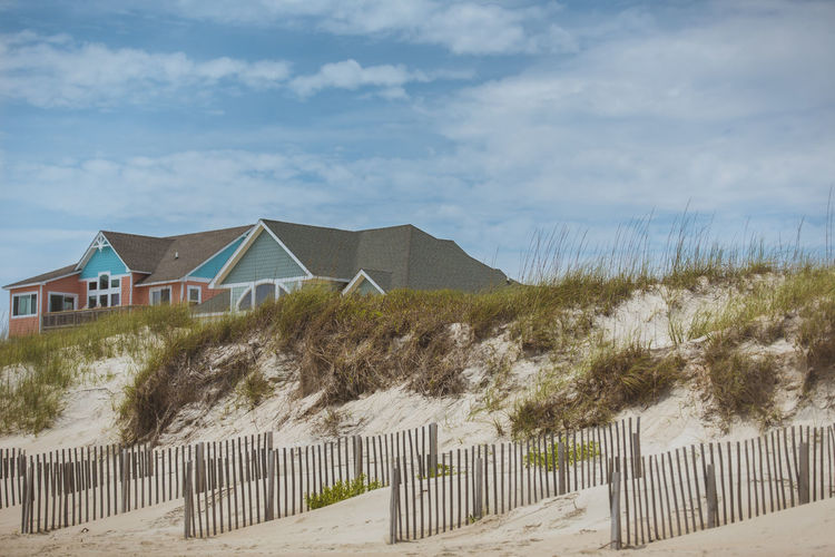 Low angle view of beach house behind sand dunes, against sky.  