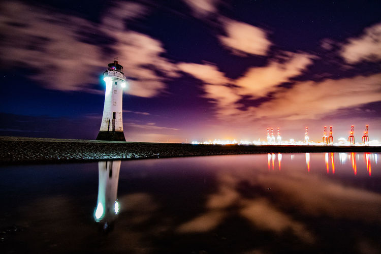 Illuminated lighthouse by sea against sky at night