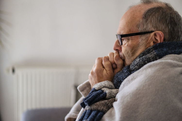 Senior man wrapped in blanket feeling cold at home