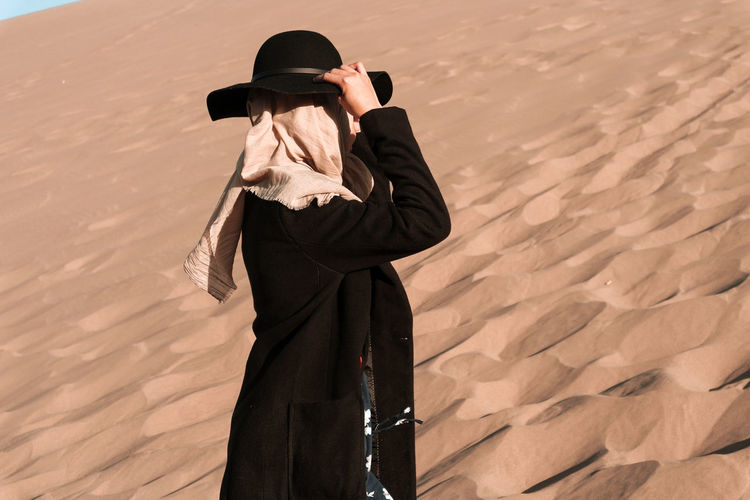 Side view of woman wearing hat and headscarf standing on sand dunes