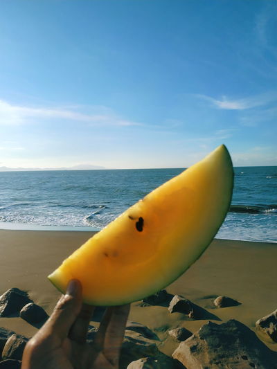 Close-up of yellow hand on beach against sky