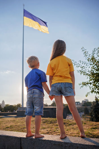Girl in yellow and boy in blue look at biggest national flag of ukraine. pray for peace and victory