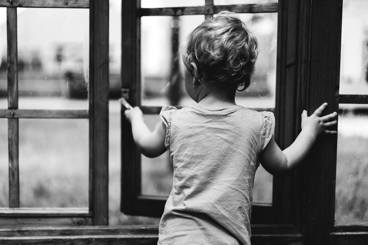 Rear view of boy standing by window