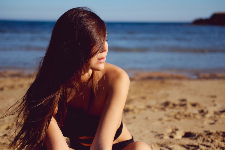 Close-up of young woman in bikini sitting at beach