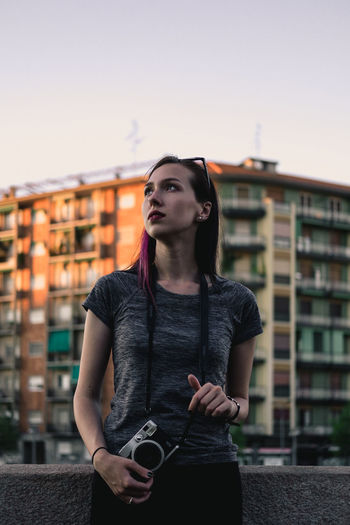 Beautiful young woman standing against sky in city