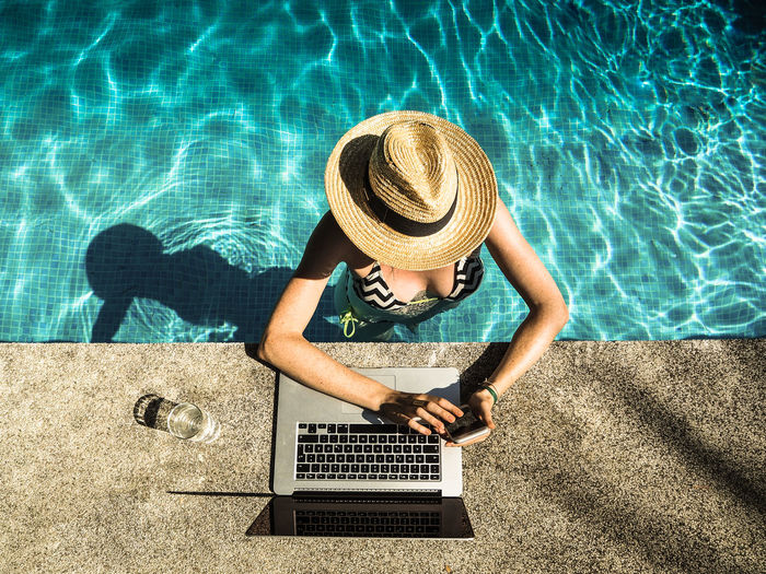 Directly above shot of woman using mobile phone by laptop at swimming pool