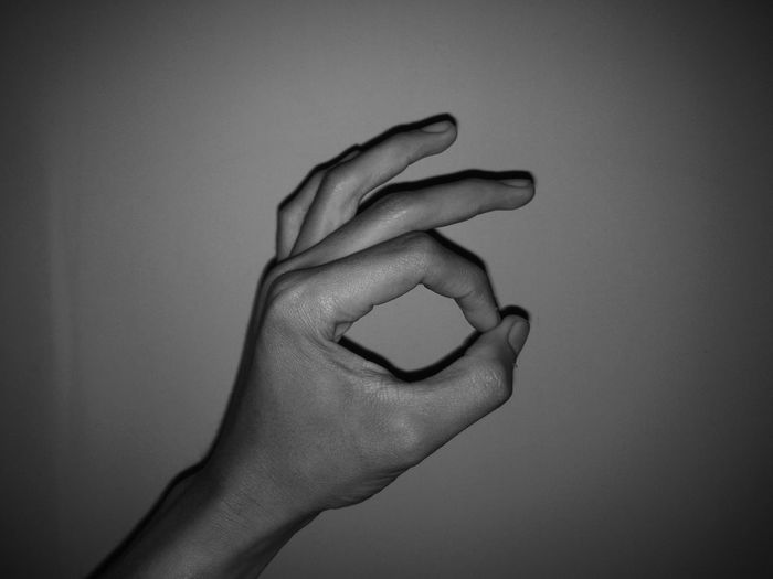 Cropped hand of person gesturing ok sign against wall