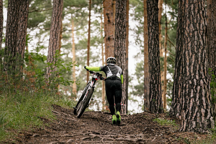Rear view of man walking with bicycle in forest