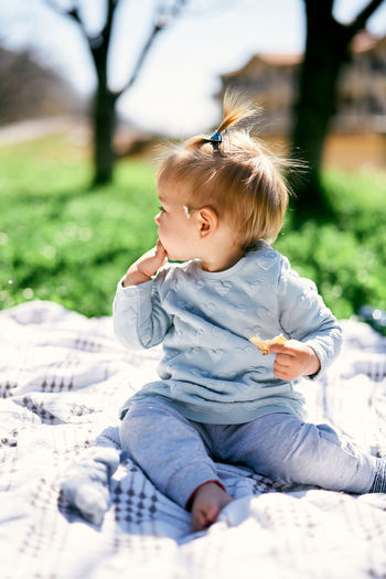 Cute baby girl sitting on grass looking away