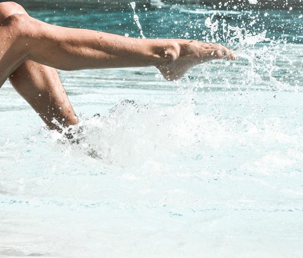 Low section of man splashing water in swimming pool