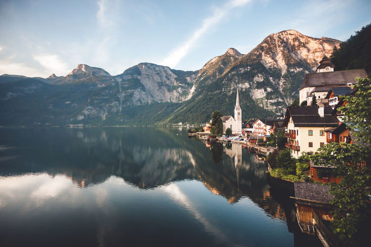 Scenic view of lake by buildings and mountains against sky