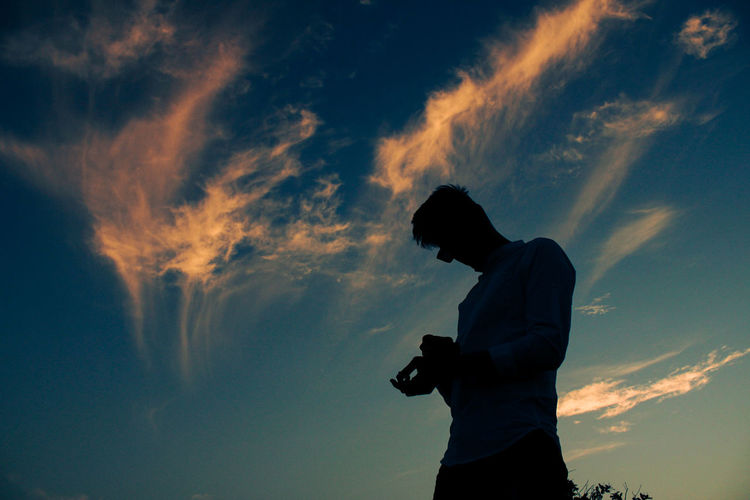 Low angle view of silhouette man using mobile phone against sky