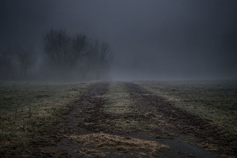 Empty dirt road against sky during foggy weather