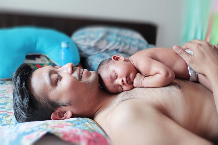 Baby sleeping over shirtless father lying on bed