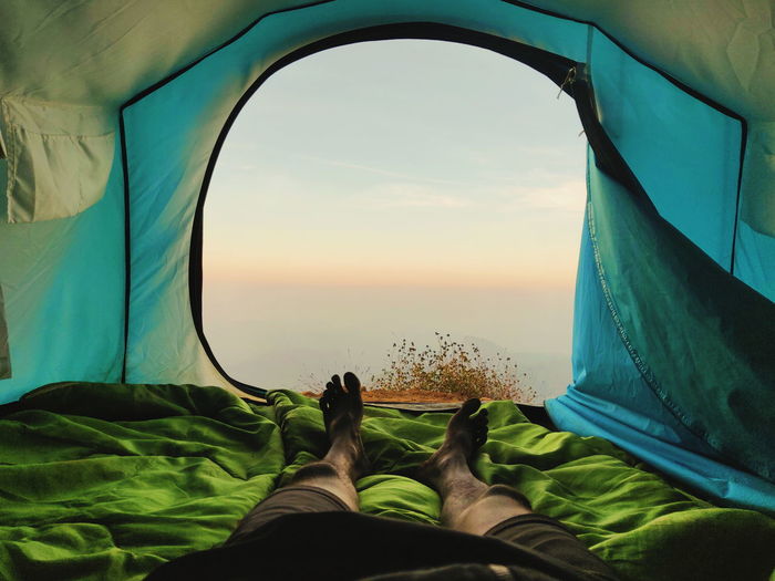 Low section of man relaxing in tent against sky during sunset
