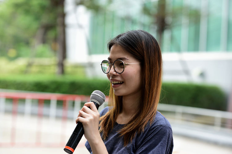Female journalist with microphone standing against building