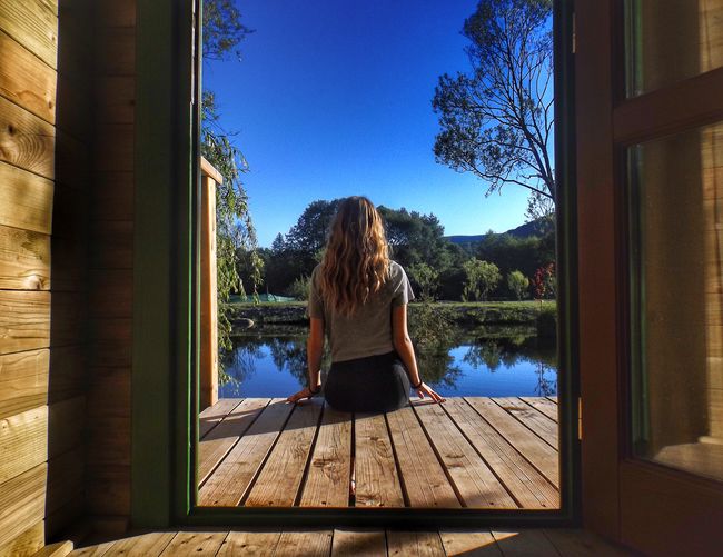 Rear view of woman sitting on pier over lake against clear blue sky