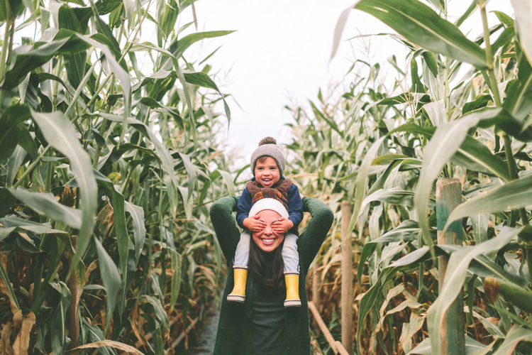 Smiling mother carrying son on shoulders amidst plants at field