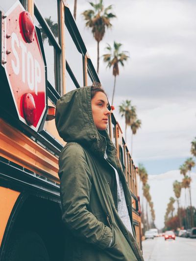 Side view of thoughtful young woman wearing jacket while standing against bus on road