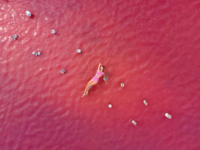 Woman in a striped bathing suit lies on a pink lake taken from above from a drone