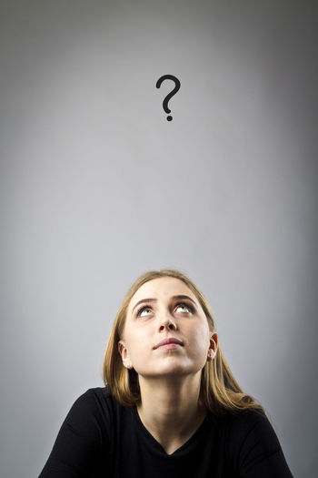 Young woman looking at question mark against gray background