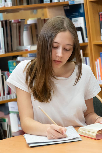 Teenage girl writing on book in library
