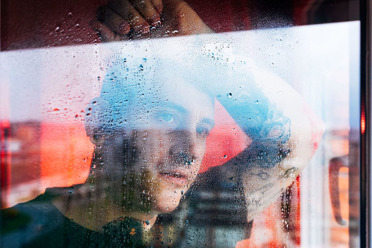 Portrait of man seen through wet glass window